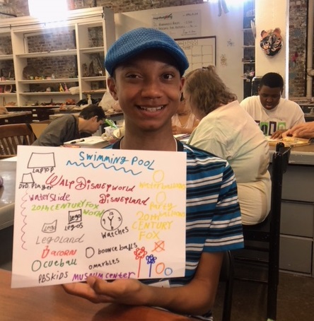 Malachi - young boy smiling and holding up his art project